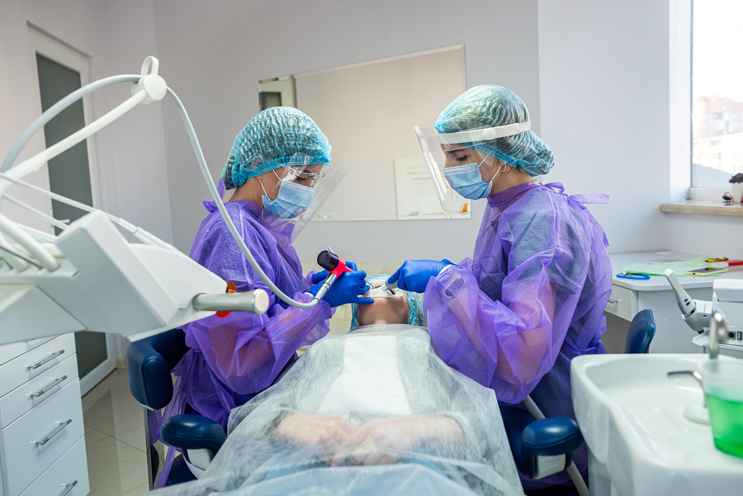two beautiful helpers in special clothes masks hats gloves help to conduct the operation to the dentist. The concept of dental surgery