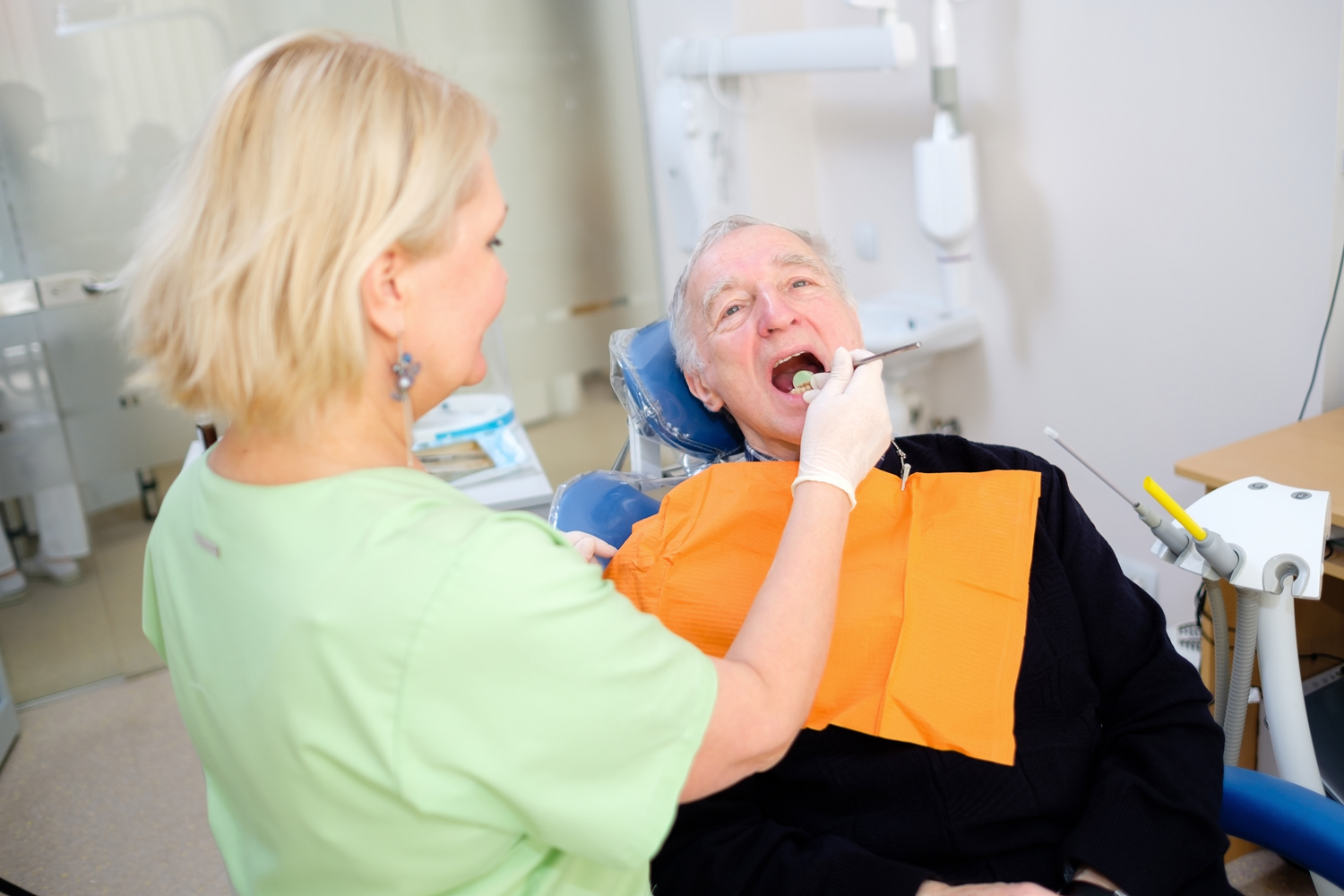 Blonde woman dentist doing dental treatment of senior male 70-75 years old patient in dental clinic. Dental care for older people. Dentistry, medicine and health care concept